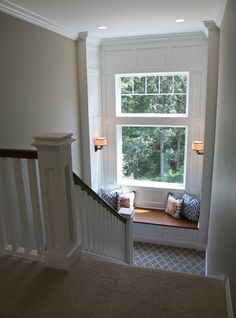 a window seat in the corner of a room next to a stair case with pillows on it