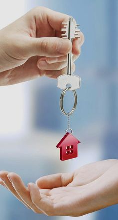 two hands are holding keys to a house shaped keychain