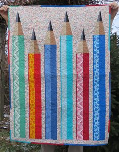 a person holding up a quilt with pencils on it