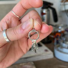 a hand holding a silver ring with two small scissors on it's end and a pair of fingers in the middle