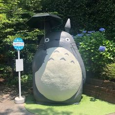 a statue of a totoro with an umbrella on it's head in front of some bushes