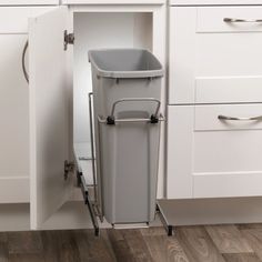 a gray trash can sitting in the middle of a white kitchen cabinet with pull out drawers