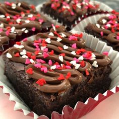 three chocolate brownies with sprinkles and hearts on them in paper cups