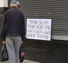 an older man standing next to a sign that says you're so in your head you can't even enjoy where you are