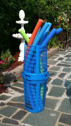 a blue basket filled with lots of different colored plastic items on top of a stone walkway