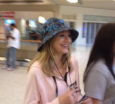 two young women standing next to each other in an airport terminal, one wearing a hat and the other holding a cell phone