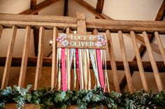 a sign hanging from the side of a wooden structure with flowers and ribbons attached to it