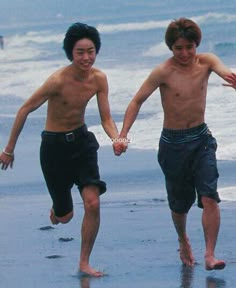 two young men running on the beach holding hands