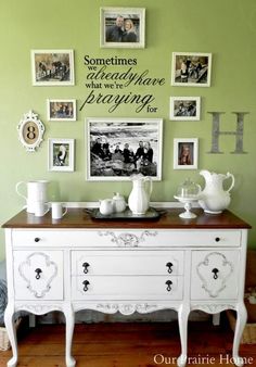 a white dresser sitting in front of a green wall with pictures on the wall above it