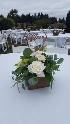 a centerpiece with white flowers and greenery on a table