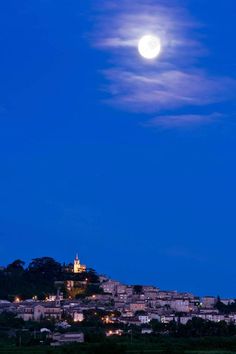 the moon is setting over a town on top of a hill