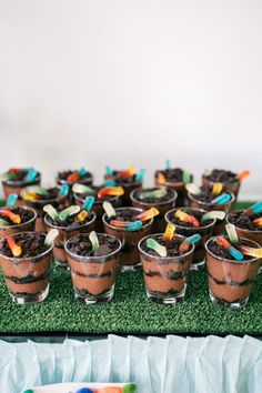 there are many desserts in small cups on the green tablecloth with candy sticks sticking out of them