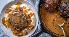 two plates filled with mashed potatoes, meatballs and gravy next to a skillet