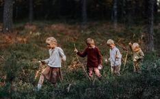 three children are walking through the woods with sticks in their hands and one child is holding something