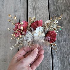 a person holding a comb with flowers and leaves on it in front of a wooden background