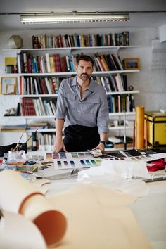 a man standing in front of a book shelf full of books and papers with his hands on the table