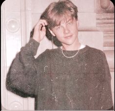 an old photo of a young man holding his hair in one hand and wearing a necklace on the other