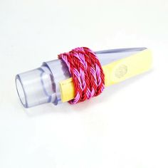 a pink and yellow cord is wrapped around a plastic tube on a white table top