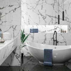 a white bath tub sitting next to a sink in a bathroom with marble walls and floors