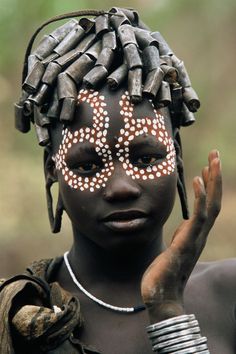 an african woman with painted face and headdress holding her hand up to the camera