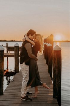 a man and woman embracing on a dock at sunset with the sun setting in the background