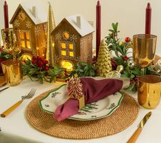 a place setting with napkins, gold candles and christmas decorations on the table in front of them