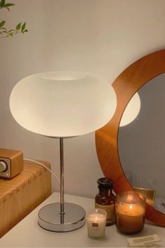 a white lamp sitting on top of a wooden table next to a mirror and candle