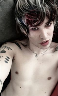 a shirtless young man with tattoos on his chest and arm is looking at the camera