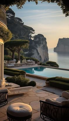 an outdoor swimming pool surrounded by greenery and stone patio furniture next to the ocean