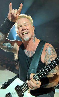 a man with tattoos on his arm and guitar in front of him, making the peace sign