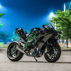 a black and green motorcycle is parked on the street in front of some trees at night