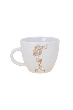 a white coffee cup with a gold mermaid design on the front and bottom, sitting on a white surface