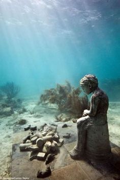 a statue sitting on top of a stone slab under water next to rocks and corals