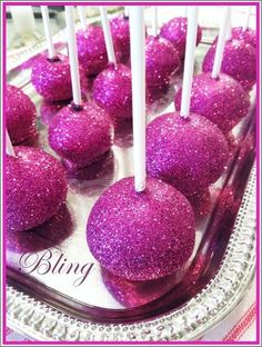 purple cake pops with white sticks in them on a tray filled with pink glittered candies