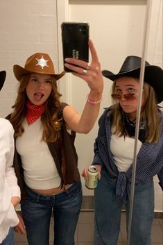 three women wearing cowboy hats taking a selfie in front of a mirror with a cell phone