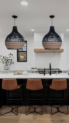 three pendant lights hanging from the ceiling above a kitchen island with stools and countertop