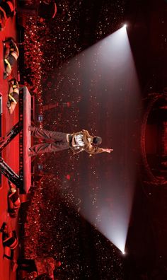 a man standing on stage with his arms out in front of the crowd and lights shining down