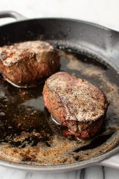 two steaks cooking in a frying pan on a stove top with oil and grease