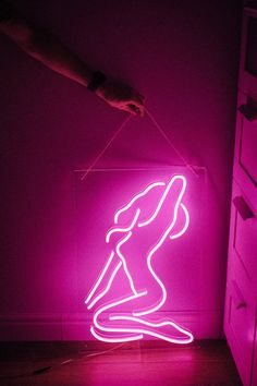 a neon sign in the shape of a woman on skis is lit up by a hand