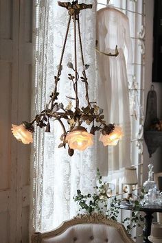 a chandelier hanging from the ceiling in front of a window with white curtains