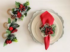 the table is set with red napkins, holly and pine cone centerpieces