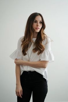 a woman in white shirt and black pants standing with her arms folded over her chest