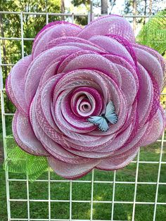 a large pink flower on top of a wire fence in the grass with a blue butterfly resting on it