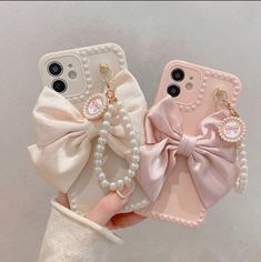 two cell phones with bows and pearls on them, one being held in the other's hand