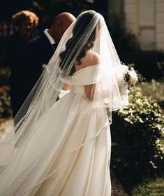 the bride and groom are walking down the path together in their wedding dresses, veils over their heads