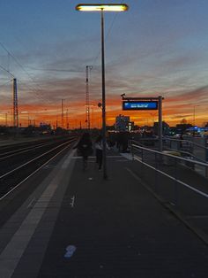 people are walking on the train tracks at sunset or dawn, as seen from an empty platform