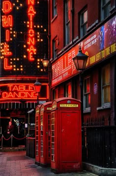 there are many red telephone booths on the side of this street that is lit up