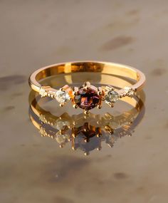 a gold ring with three different colored stones on the top and bottom, sitting on a reflective surface