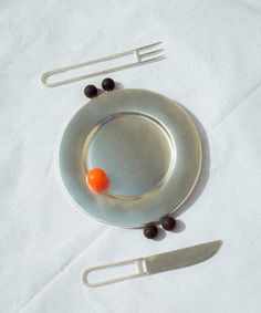 a plate with an orange ball on it next to utensils and a knife