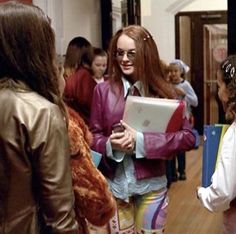 a group of young women standing around each other in a hallway with one woman holding a laptop